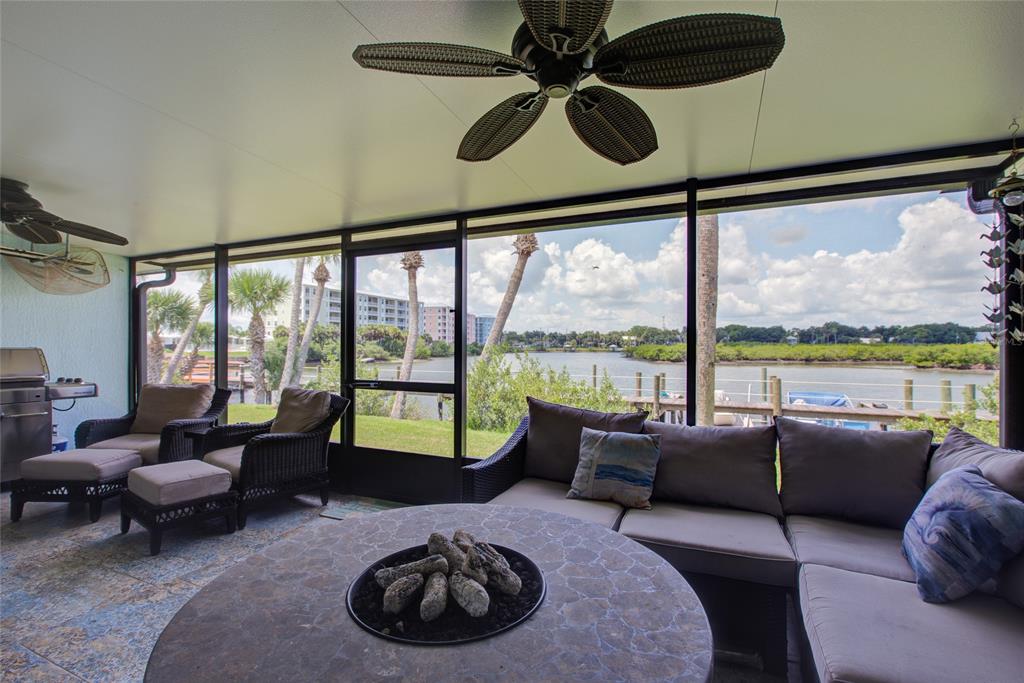 A screened-in patio features wicker furniture, a fire pit table, and views of a waterway — 58 SABAL CAY COURT, NEW SMYRNA BEACH, FL