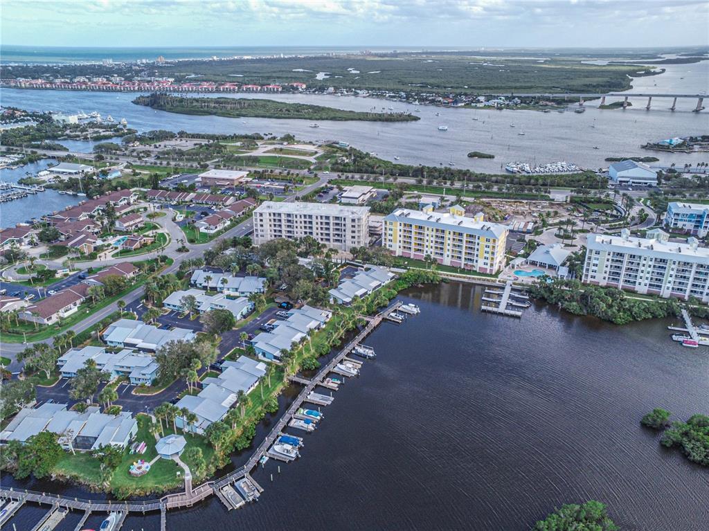 An aerial view shows waterfront condominiums, a boat dock, and a bridge over the bay — 58 SABAL CAY COURT, NEW SMYRNA BEACH, FL
