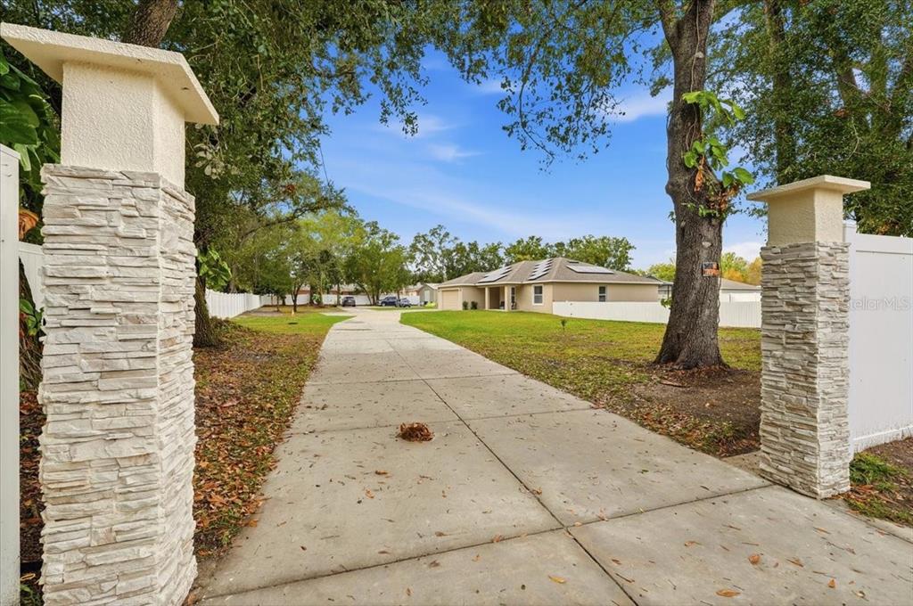A concrete driveway leads through stone pillars toward a single-story house with solar panels — 31 MORGAN STREET, AUBURNDALE, FL