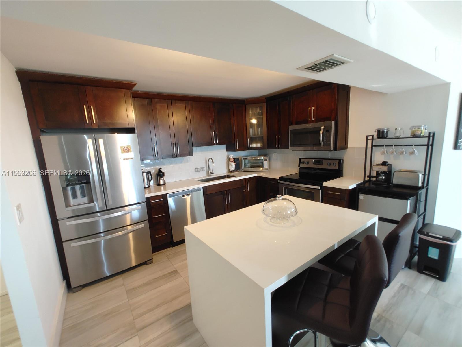 A kitchen features dark wood cabinets, stainless steel appliances, and a white island with seating — 7135 Collins Ave # 525, Miami Beach FL 33141, MIAMI BEACH, FL