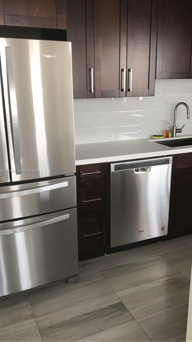 A modern kitchen features dark wood cabinets, stainless steel appliances, and light gray tile flooring — 7135 Collins Ave # 525, Miami Beach FL 33141, MIAMI BEACH, FL