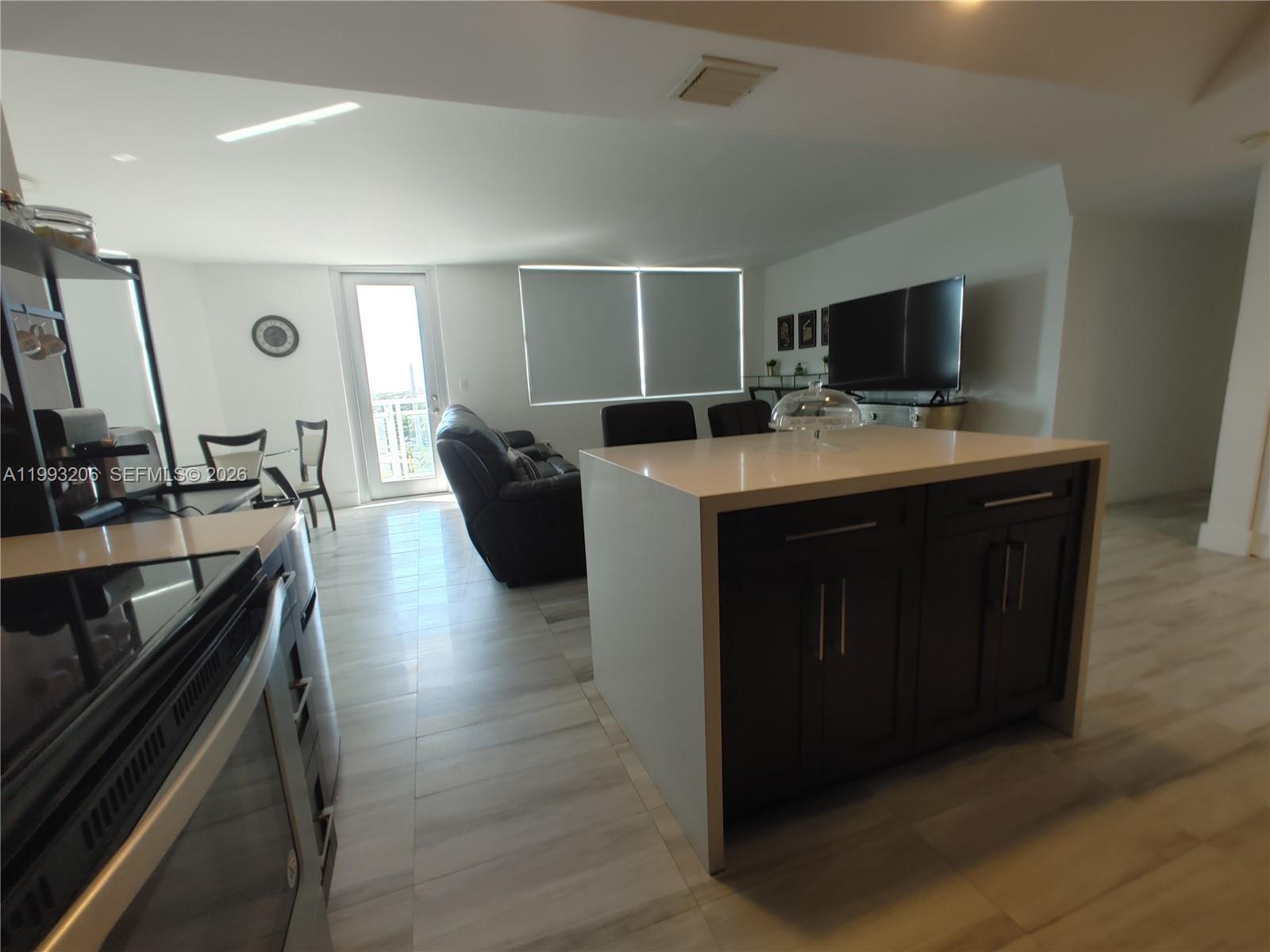 A kitchen island with dark cabinets and a white countertop sits in an open-concept living area — 7135 Collins Ave # 525, Miami Beach FL 33141, MIAMI BEACH, FL