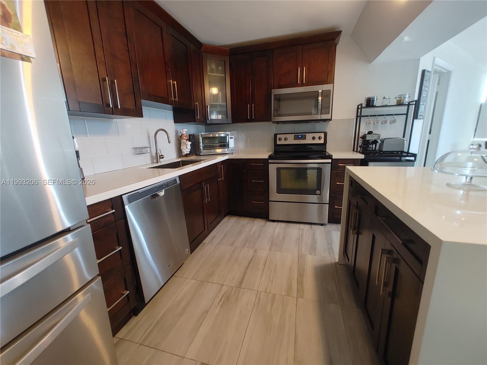 A kitchen features dark wood cabinets, stainless steel appliances, and white countertops — 7135 Collins Ave # 525, Miami Beach FL 33141, MIAMI BEACH, FL
