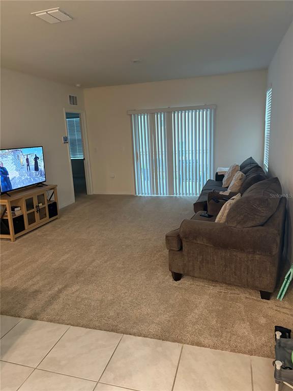 A living room features beige carpeting, a grey sofa, a television on a stand, and sliding glass doors — 1360 BERRY LANE, DAVENPORT, FL