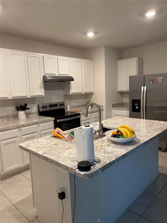 A kitchen features white cabinets, a granite-look island with a sink, and stainless steel appliances — 1360 BERRY LANE, DAVENPORT, FL