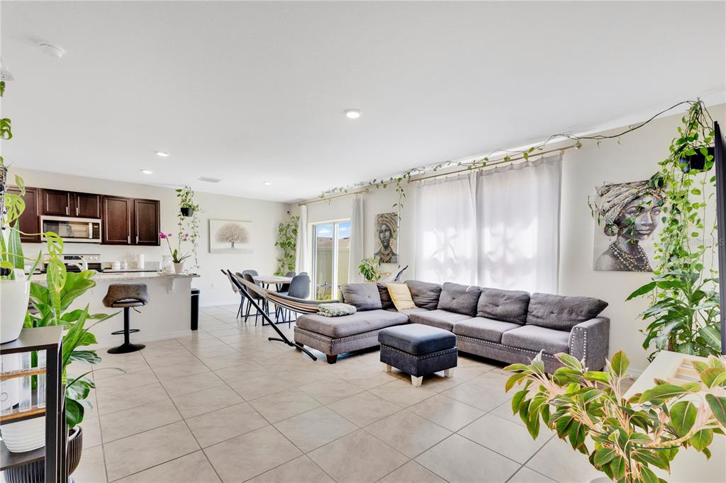 An open-concept living room and kitchen featuring tile floors, a gray sectional, and hanging plants — 831 TURNER LANE, WINTER HAVEN, FL