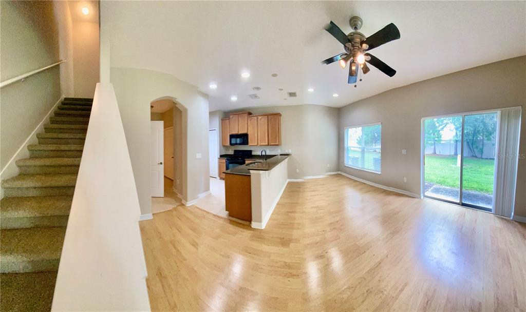 An open-concept living area features light wood flooring, a kitchen with wood cabinets, and stairs — 2413 HARLEYFORD PLACE, CASSELBERRY, FL