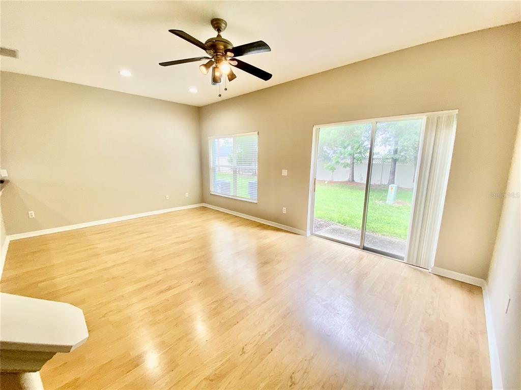 An empty living room features light wood flooring, a ceiling fan, and sliding glass patio doors — 2413 HARLEYFORD PLACE, CASSELBERRY, FL