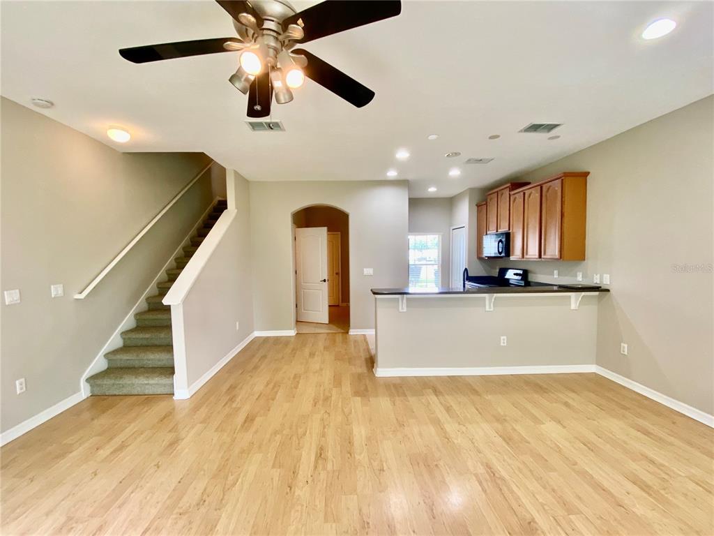 An open-concept living area features light wood flooring, a carpeted staircase, and a kitchen breakfast bar — 2413 HARLEYFORD PLACE, CASSELBERRY, FL