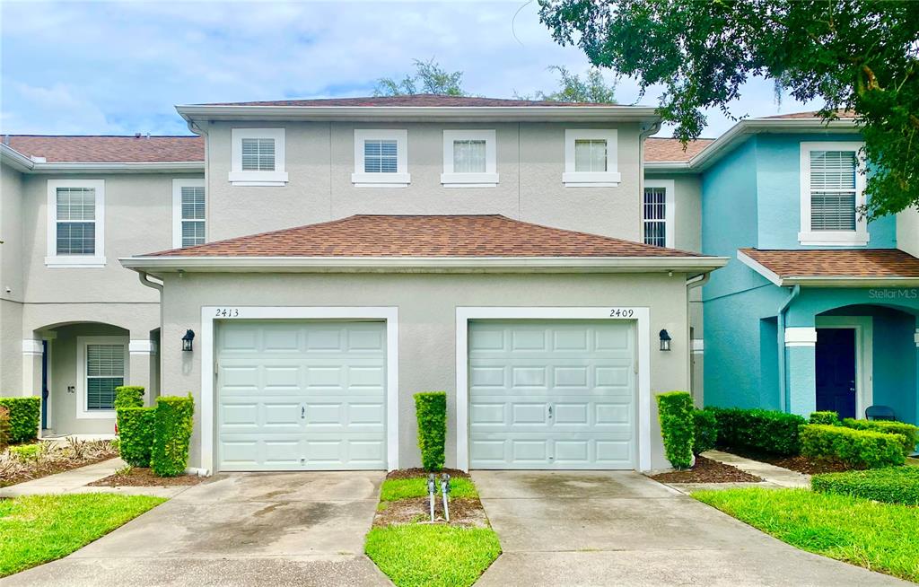 The exterior of a two-story townhouse featuring two garage doors and light-colored stucco siding — 2413 HARLEYFORD PLACE, CASSELBERRY, FL
