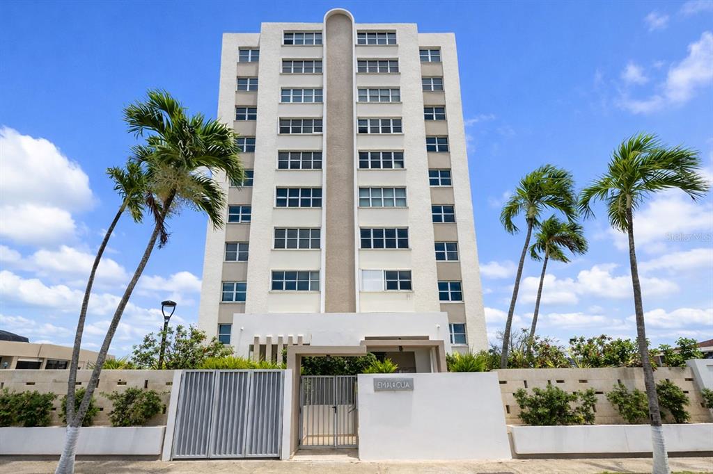 A multi-story white apartment building stands behind a gated entrance with palm trees — 9 EMAJAGUA UNIT 7B, SAN JUAN, PR