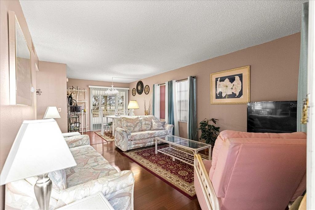 A living room with floral sofas, a pink armchair, a glass coffee table, and wood flooring — 7885 MIDWAY DRIVE TERRACE UNIT E101, OCALA, FL