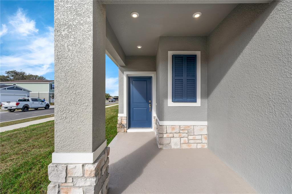 A covered front porch features a blue door, stone accents, and recessed ceiling lighting — 4462 RIVER BEACON BOULEVARD, DAVENPORT, FL