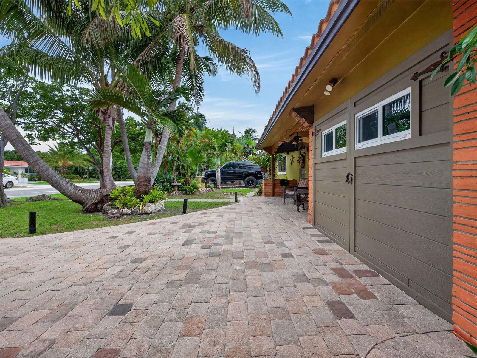 A paved driveway leads to a house with brown garage doors and a brick exterior — 949 NE 25th Avenue, Pompano Beach FL 33062, POMPANO BEACH, FL