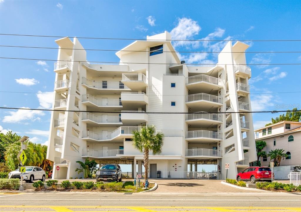 A multi-story white residential building with balconies and a parking area at ground level — 10116 GULF BOULEVARD UNIT 203W, TREASURE ISLAND, FL