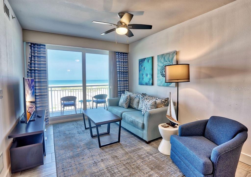 A living room features a blue sofa, an armchair, and a balcony overlooking the ocean — 10116 GULF BOULEVARD UNIT 203W, TREASURE ISLAND, FL