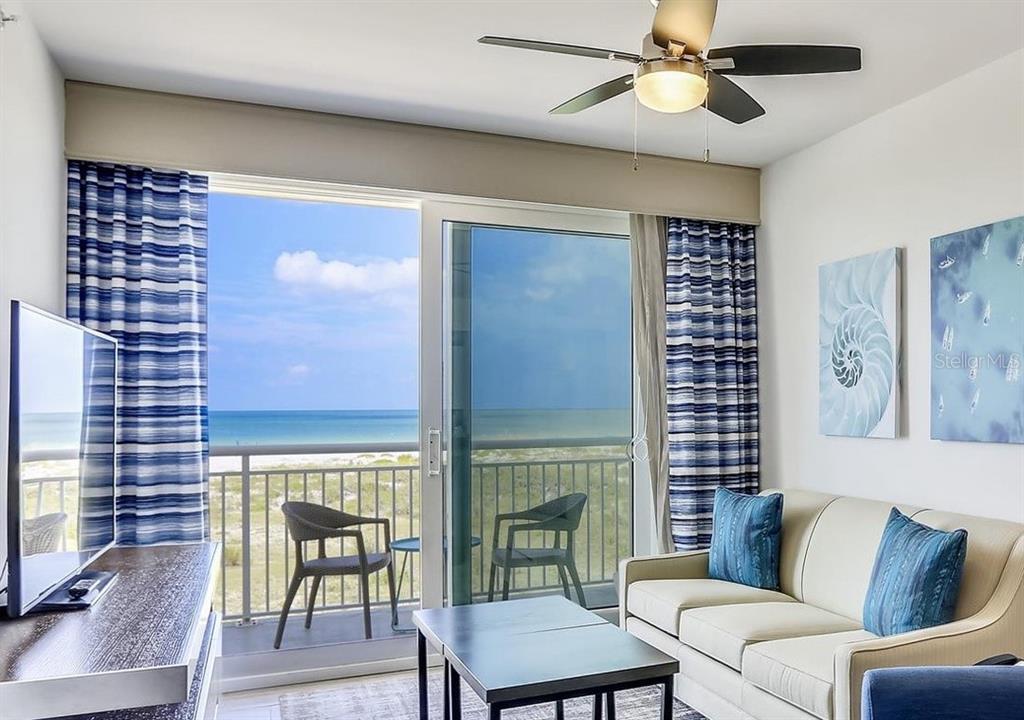 A living room features a sofa, television, and sliding glass doors opening to a beach balcony — 10116 GULF BOULEVARD UNIT 203W, TREASURE ISLAND, FL