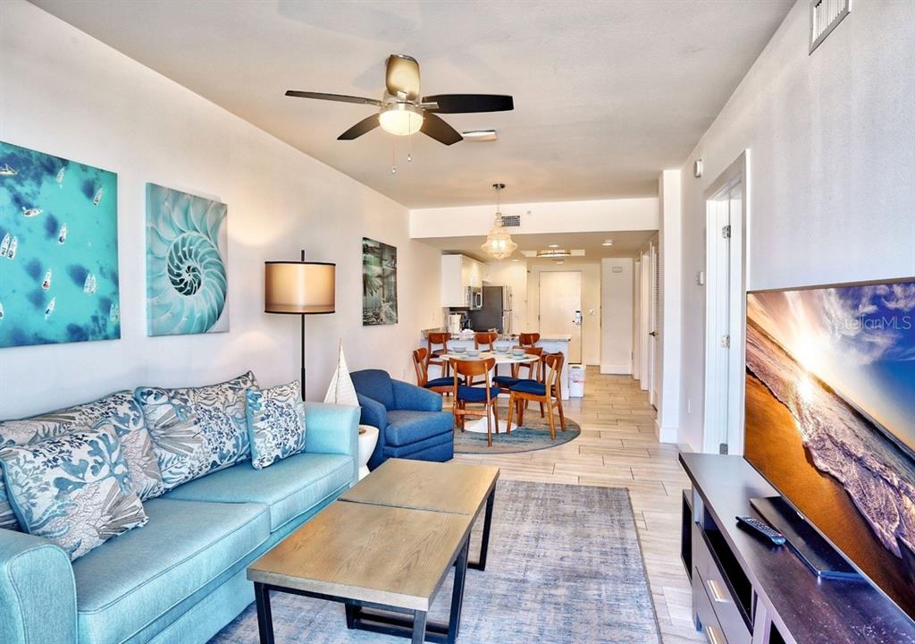 A living room and dining area feature light tile floors, blue furniture, and coastal decor — 10116 GULF BOULEVARD UNIT 203W, TREASURE ISLAND, FL