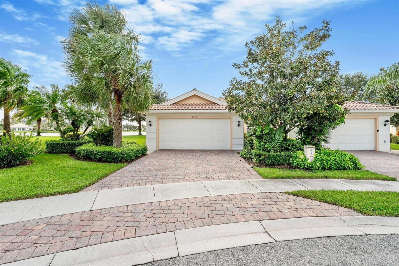 A single-story house with a two-car garage, brick paver driveway, and lush landscaping — 8270 Eleuthera Lane, Wellington FL 33414, WELLINGTON, FL