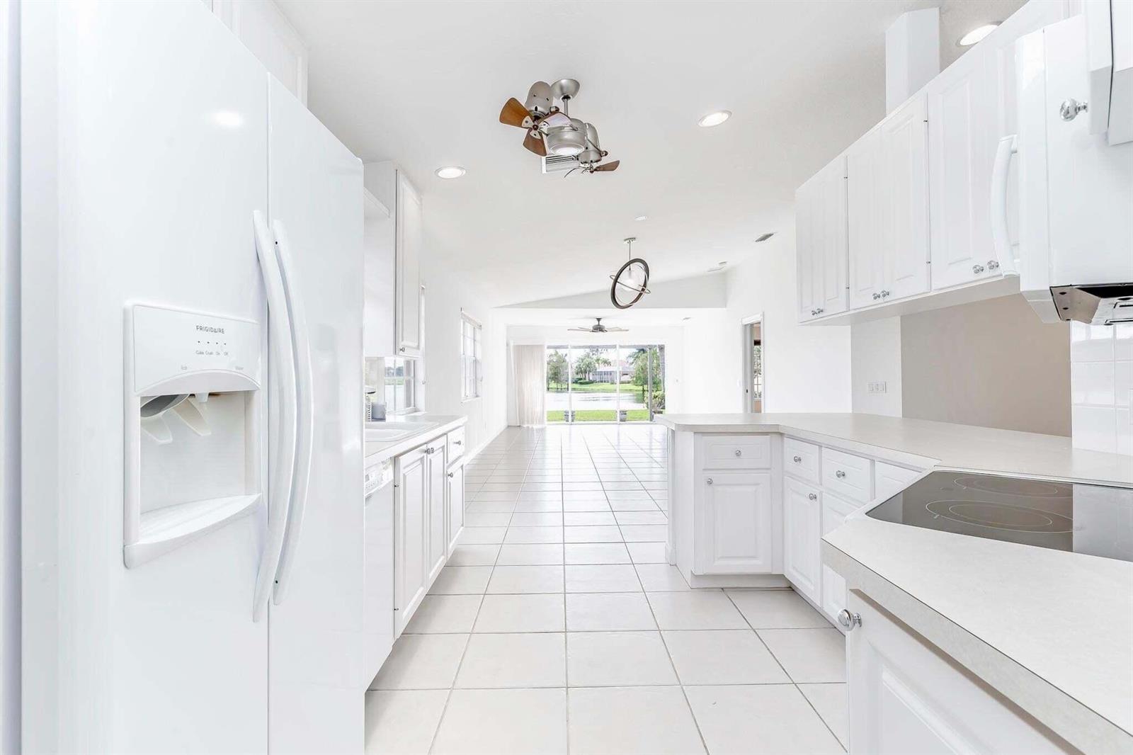 A white kitchen with tile floors leads to an open living area with lake views — 8270 Eleuthera Lane, Wellington FL 33414, WELLINGTON, FL