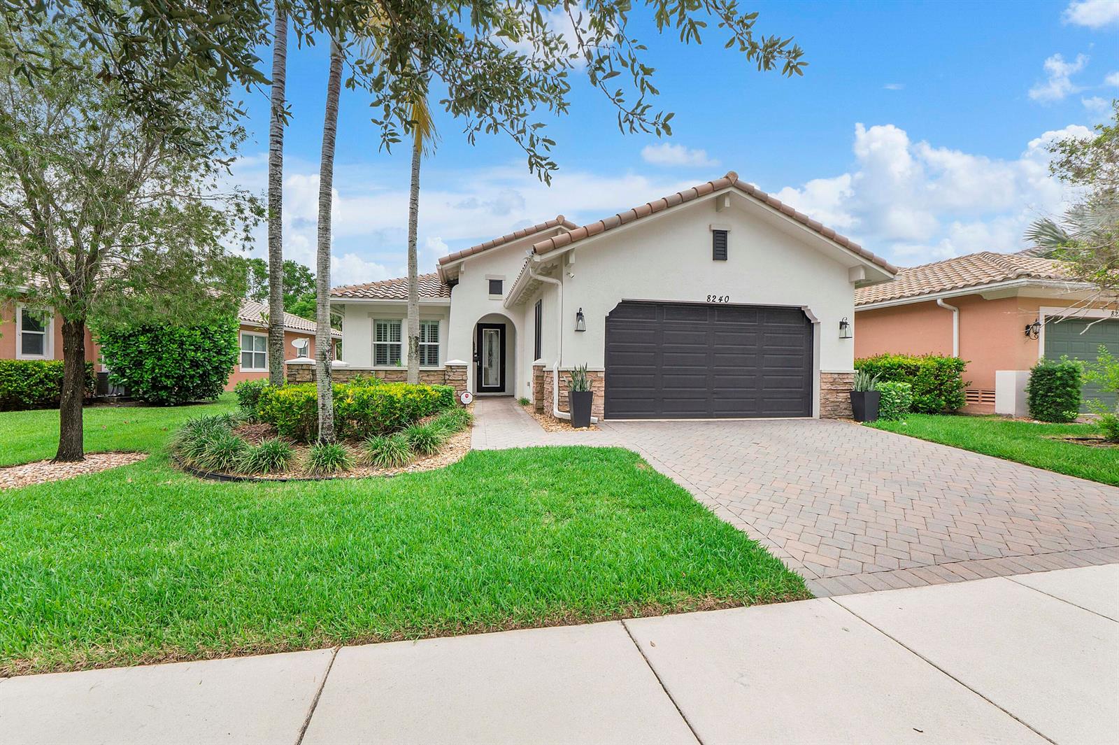 A single-story house with a paved driveway, a dark garage door, and a tiled roof — 8240 NW 120th Way, Parkland FL 33076, PARKLAND, FL