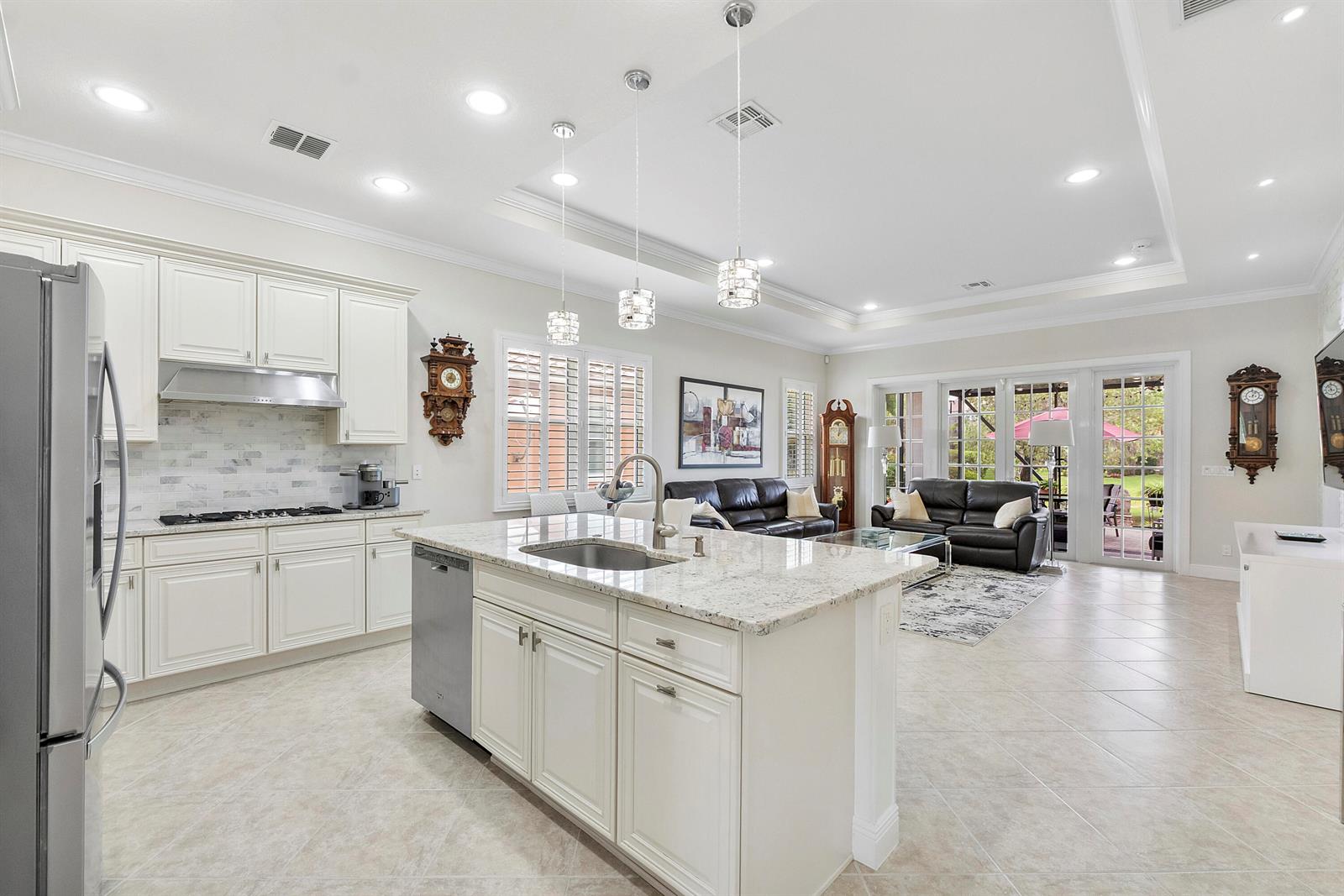 A kitchen with white cabinets and a granite island opens into a living room area — 8240 NW 120th Way, Parkland FL 33076, PARKLAND, FL