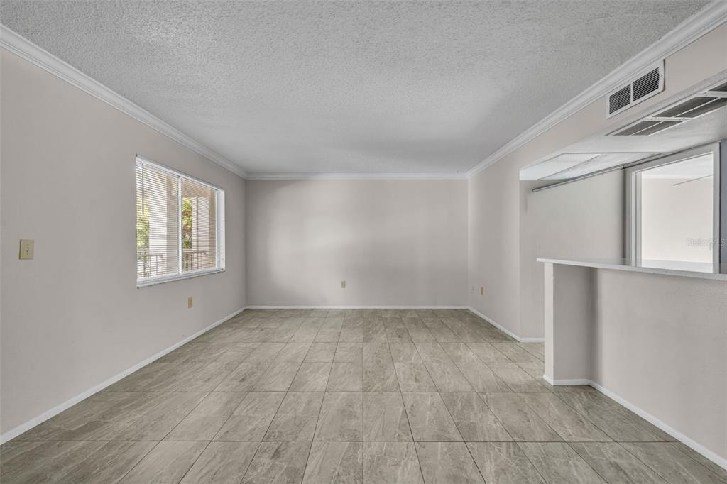 An empty living room features light-colored tile flooring, neutral walls, and a breakfast bar opening — 145 OYSTER BAY CIRCLE UNIT 240, ALTAMONTE SPRINGS, FL