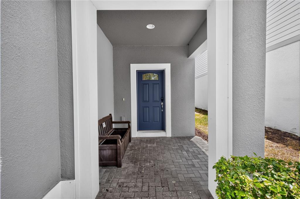 A covered entryway features a blue front door, a wooden bench, and paver flooring — 8922 ZURICH LANE, KISSIMMEE, FL
