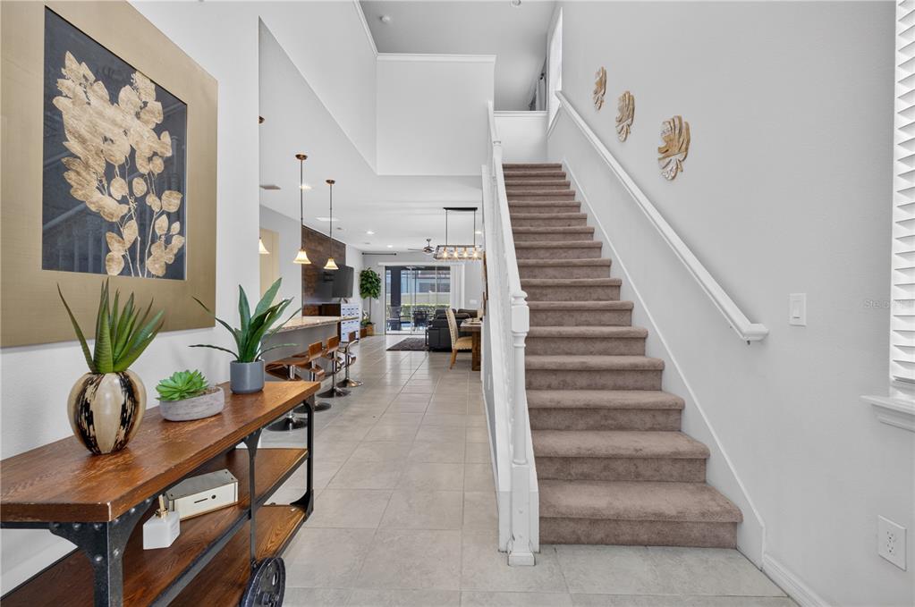 A foyer with a wooden console table leads to a carpeted staircase and open kitchen — 8922 ZURICH LANE, KISSIMMEE, FL