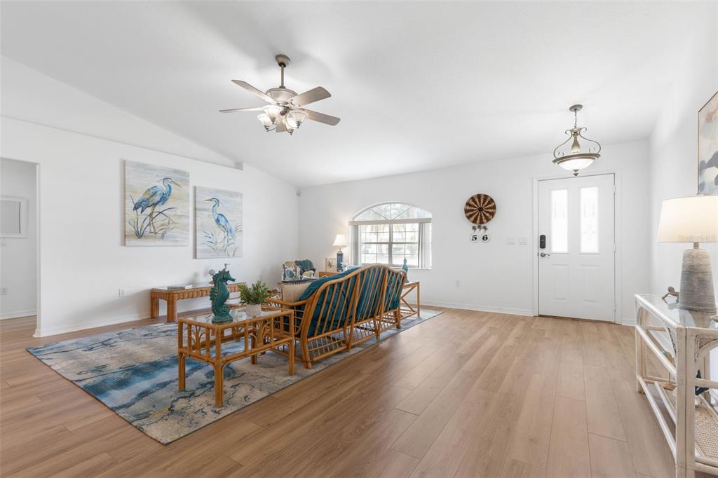 A bright living room features light wood flooring, a ceiling fan, and coastal-themed wall art — 56 PRITCHARD DRIVE, PALM COAST, FL