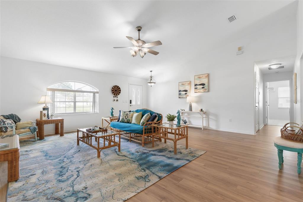 A bright living room features light wood flooring, a blue area rug, and rattan furniture — 56 PRITCHARD DRIVE, PALM COAST, FL