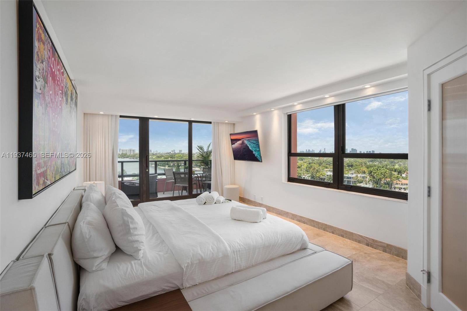 A modern bedroom features a king bed, large windows with city views, and a private balcony — 5225 Collins Ave # 1221, Miami Beach FL 33140, MIAMI BEACH, FL