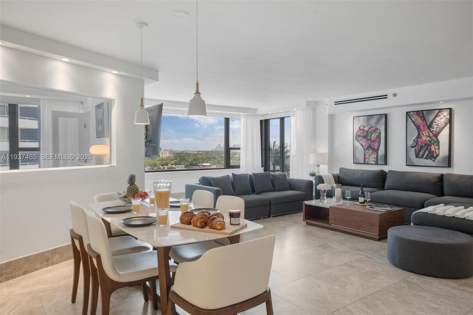 A modern open-concept living and dining area features tile floors, gray sofas, and city views — 5225 Collins Ave # 1221, Miami Beach FL 33140, MIAMI BEACH, FL