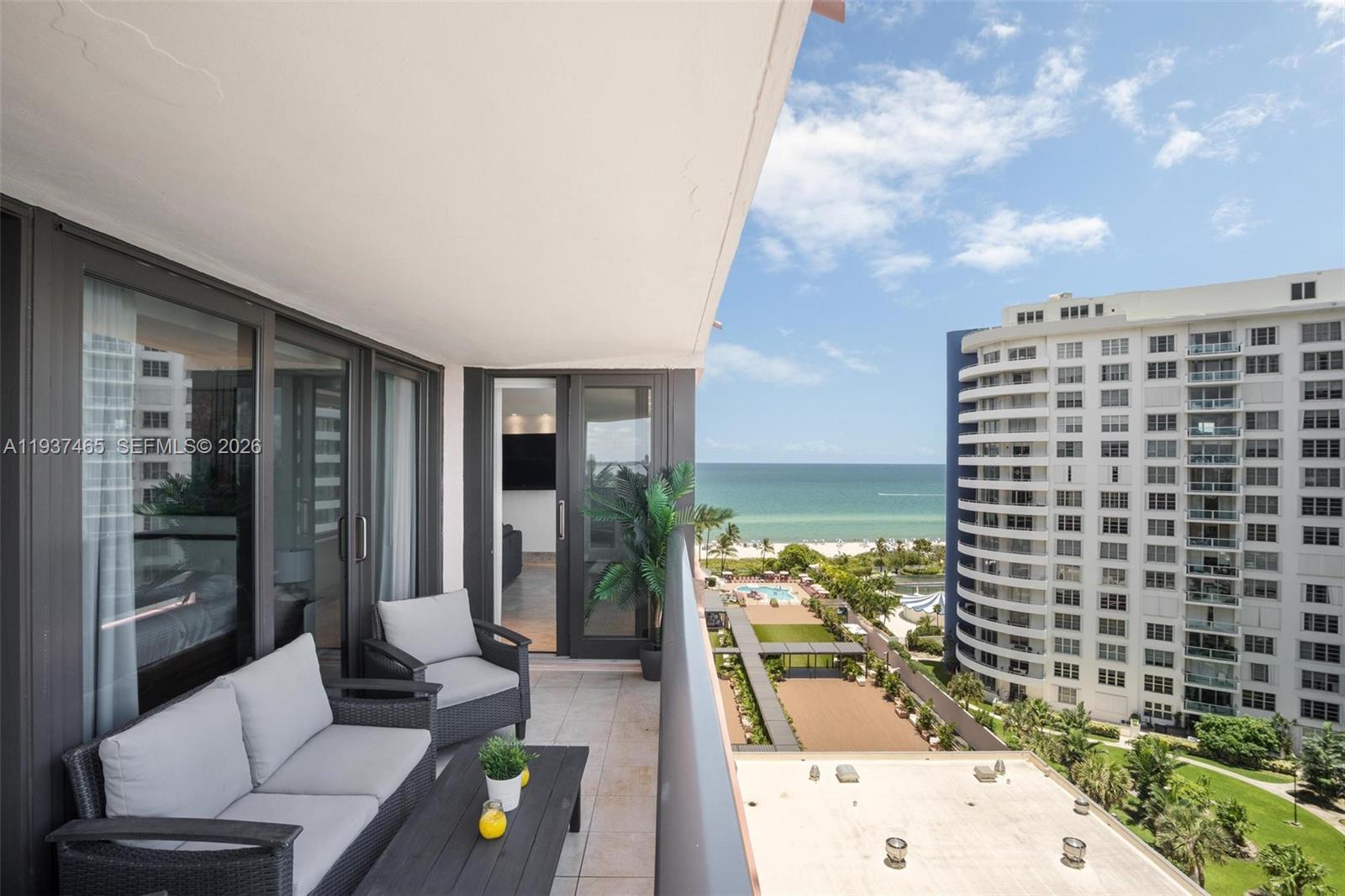 A balcony with outdoor furniture overlooks a swimming pool, beach, and a high-rise building — 5225 Collins Ave # 1221, Miami Beach FL 33140, MIAMI BEACH, FL
