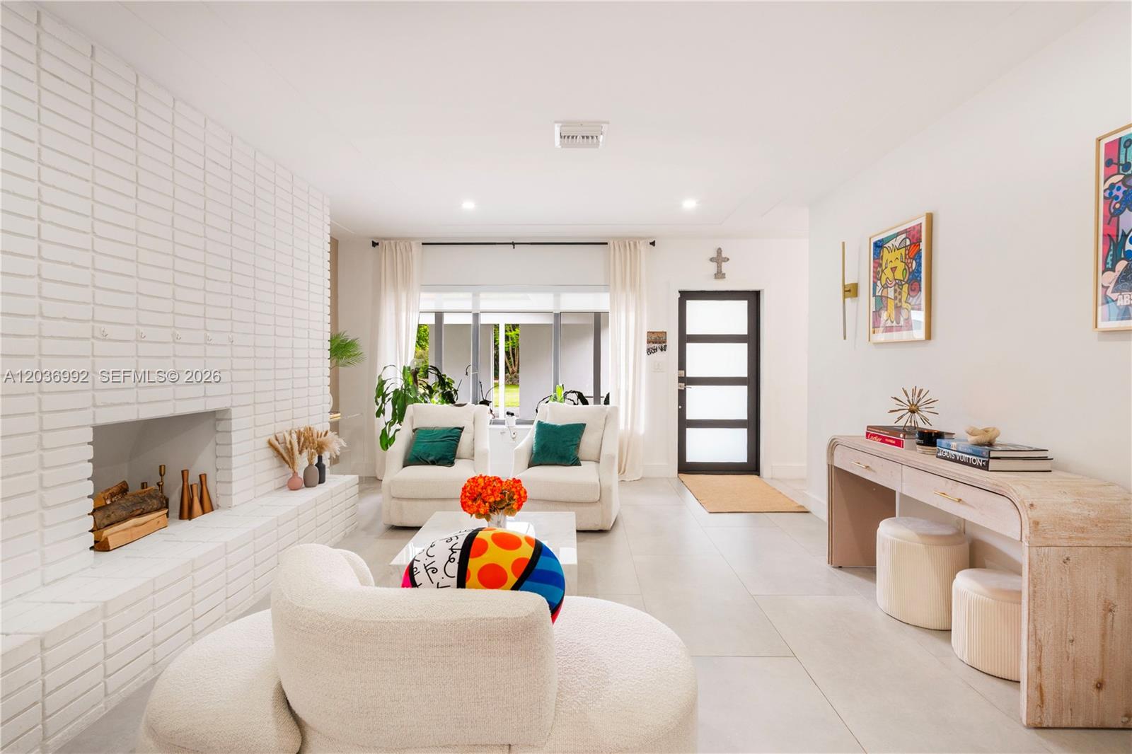 A bright living room features a white brick fireplace, modern furniture, and a glass-paneled door — 7970 SW 122nd St, Pinecrest FL 33156, PINECREST, FL