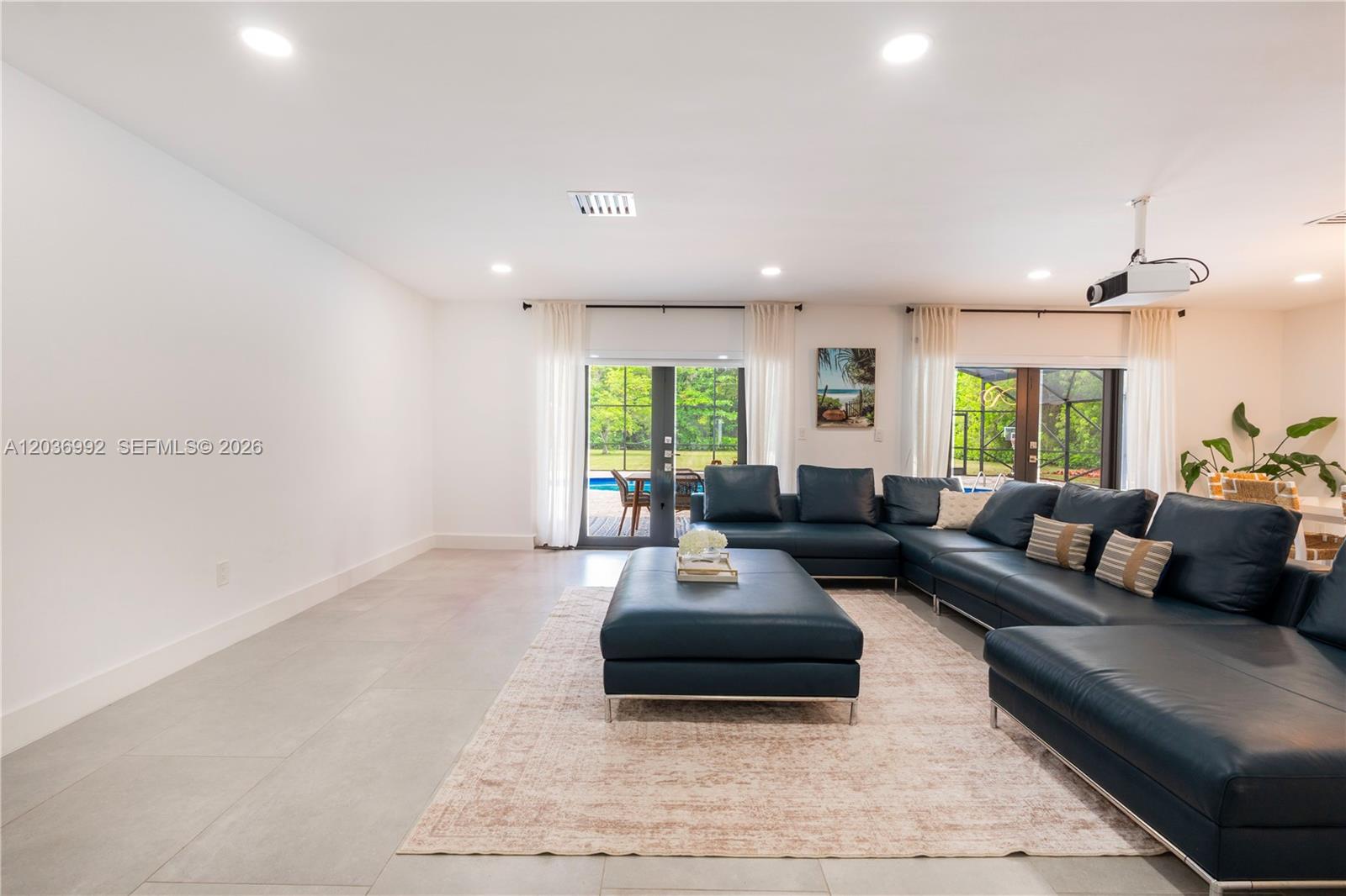 A living room features a large blue sectional sofa, a matching ottoman, and glass doors — 7970 SW 122nd St, Pinecrest FL 33156, PINECREST, FL