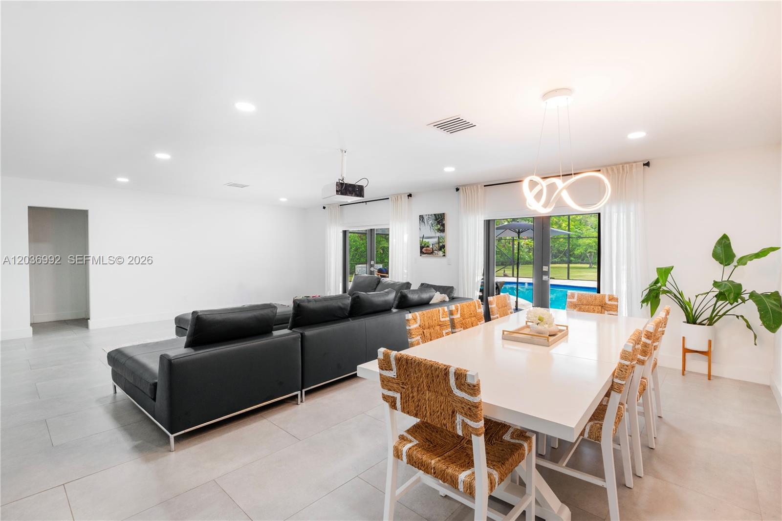 A bright open-concept living and dining area features a black sectional, white table, and pool view — 7970 SW 122nd St, Pinecrest FL 33156, PINECREST, FL