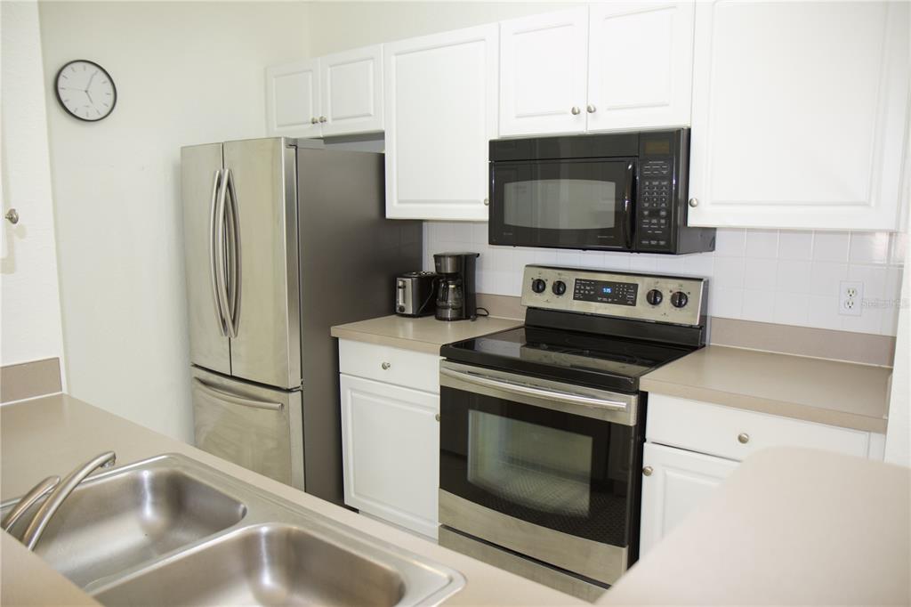 A kitchen features white cabinets, stainless steel appliances, a double sink, and beige countertops — 4323 BAYSIDE VILLAGE DRIVE UNIT 306, TAMPA, FL