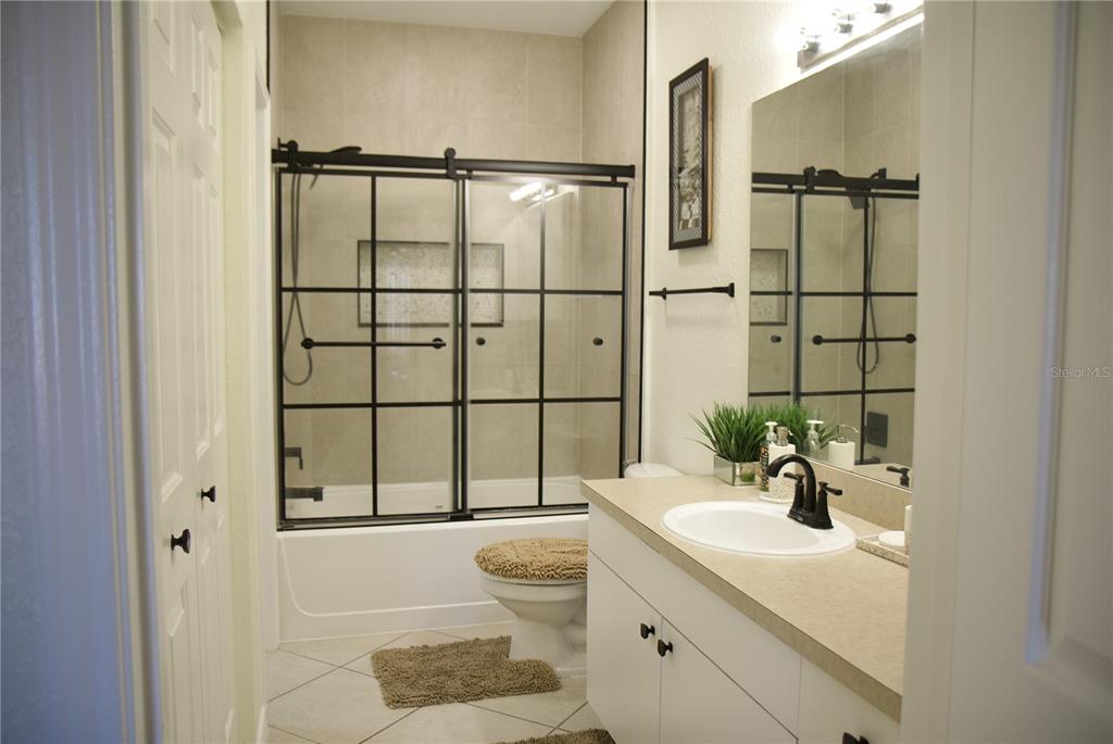 A bathroom features a white vanity, a toilet with a fuzzy cover, and a glass-enclosed tub — 4323 BAYSIDE VILLAGE DRIVE UNIT 306, TAMPA, FL