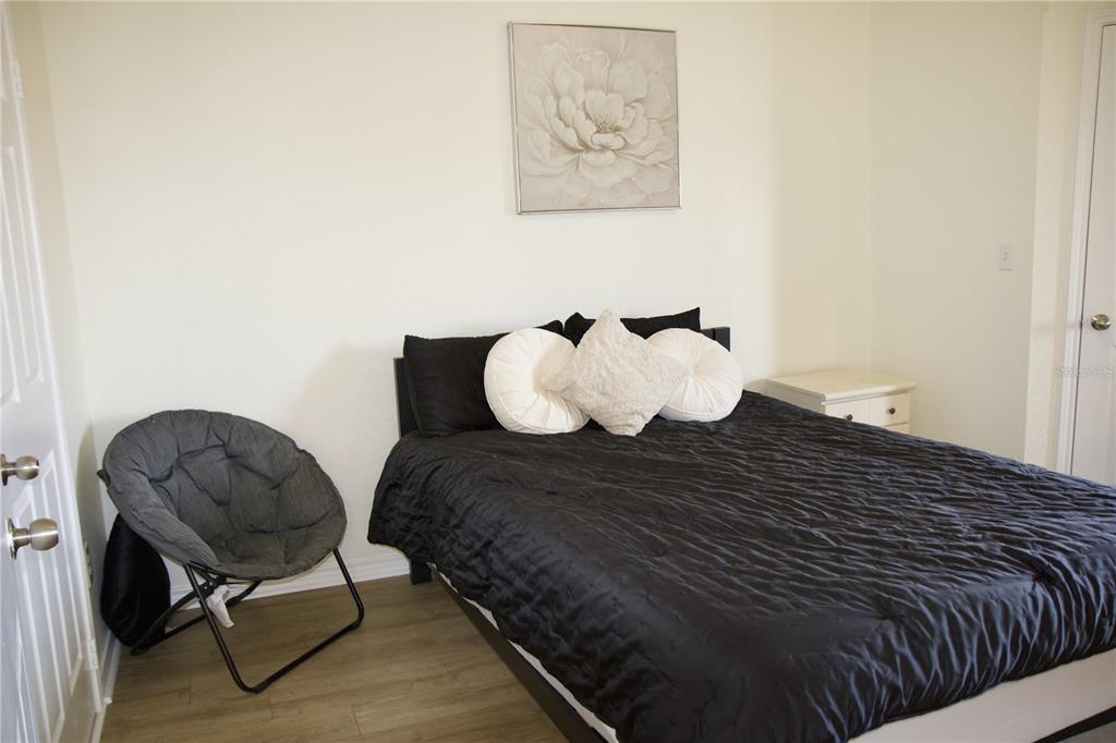A bedroom features a bed with black bedding, a gray saucer chair, and wall art — 4323 BAYSIDE VILLAGE DRIVE UNIT 306, TAMPA, FL