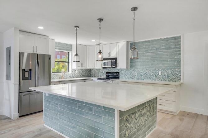 A modern kitchen features white cabinets, a large island, and blue-green subway tile backsplashes — 360 Wilma Circle # 7, Riviera Beach FL 33404, RIVIERA BEACH, FL