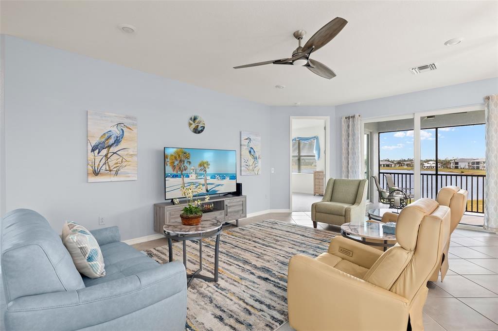A living room features a blue sofa, two beige recliners, and a view of a lake — 14150 POPPY FIELD LOOP UNIT 4322, PUNTA GORDA, FL