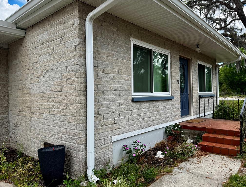 A tan brick house exterior features a blue front door, white downspout, and tiled steps — 34817 ORCHID PARKWAY, DADE CITY, FL