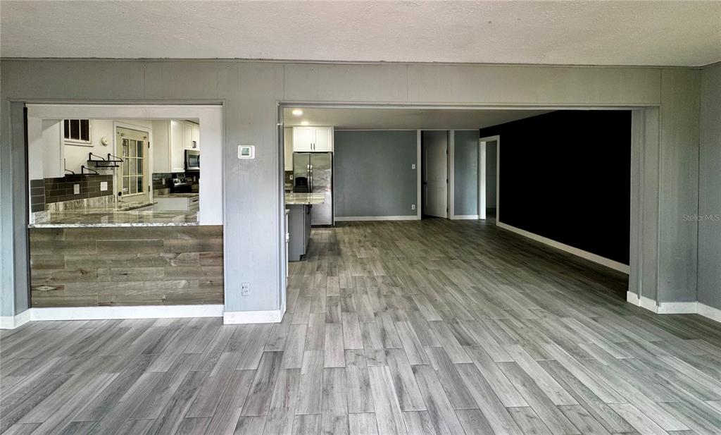 An open-concept living area features gray wood-look flooring and a kitchen with a pass-through window — 34817 ORCHID PARKWAY, DADE CITY, FL
