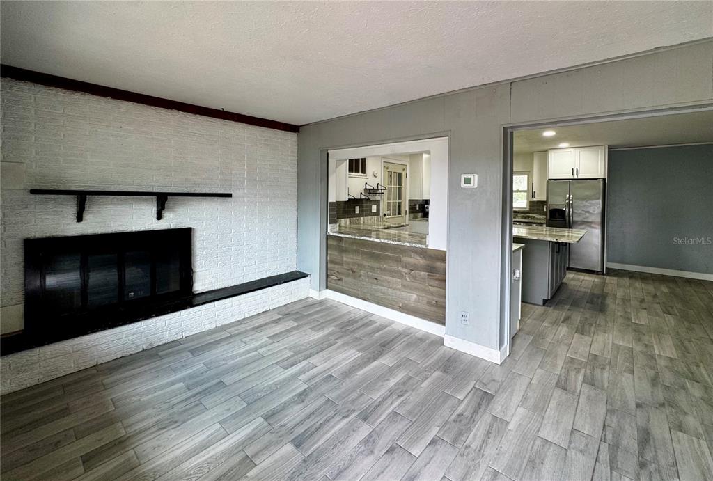 A living room features a white brick fireplace, wood-look tile flooring, and a kitchen pass-through — 34817 ORCHID PARKWAY, DADE CITY, FL
