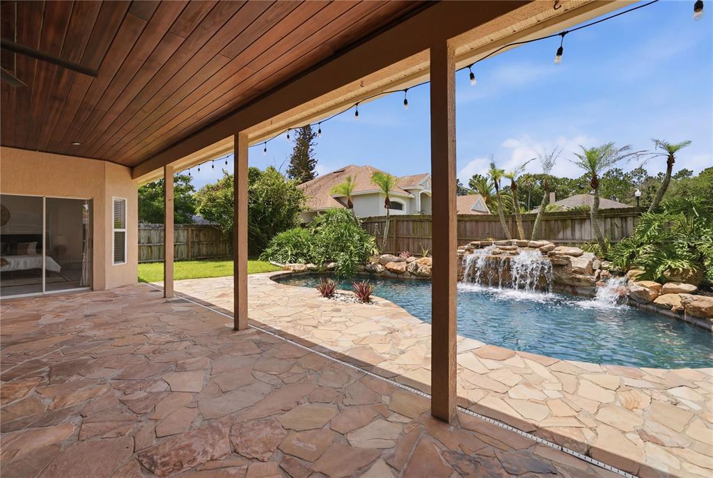 A stone patio with a covered wooden ceiling overlooks a swimming pool with a waterfall — 13000 CRYSTAL COVE DRIVE, ORLANDO, FL