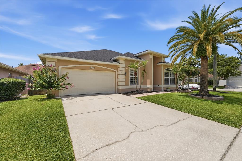 A single-story tan house with a two-car garage, a palm tree, and a concrete driveway — 13000 CRYSTAL COVE DRIVE, ORLANDO, FL