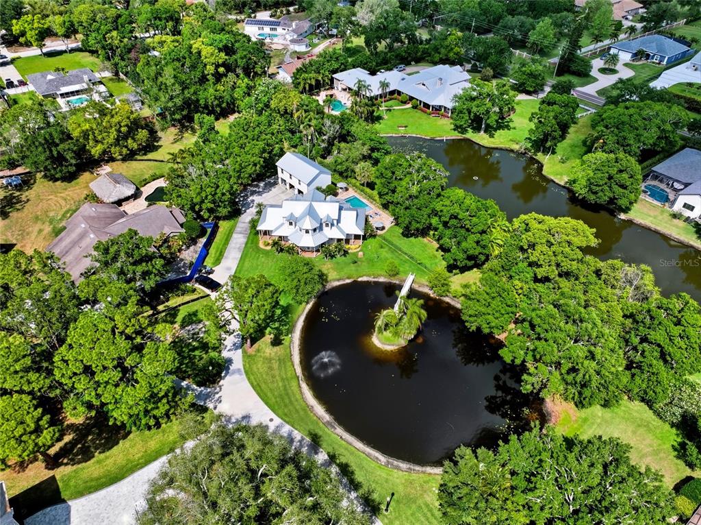 An aerial view shows a large house with a pool and pond on a wooded lot — 13227 110TH AVENUE, LARGO, FL