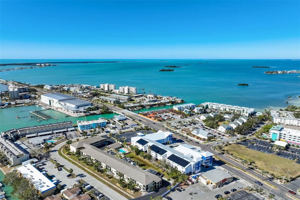 An aerial view shows a coastal community with multi-story buildings, parking lots, and surrounding water — 460 S PAULA DRIVE UNIT 108, DUNEDIN, FL