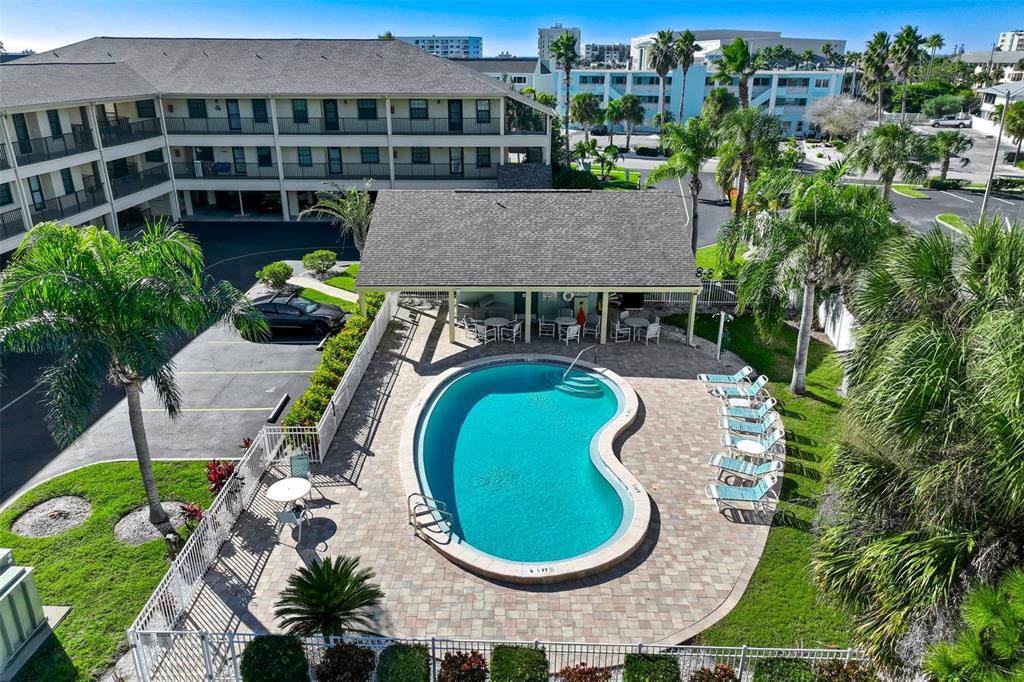 An aerial view of a kidney-shaped swimming pool with a covered patio and lounge chairs — 460 S PAULA DRIVE UNIT 108, DUNEDIN, FL
